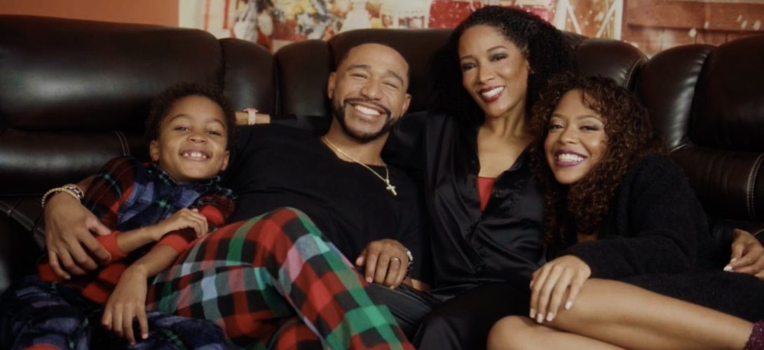 A heartwarming scene from A Christmas Miracle featuring a smiling family of four sitting together on a cozy couch.