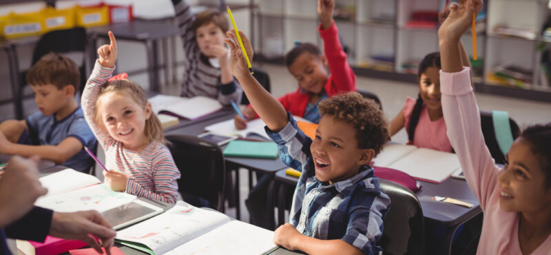Schoolkids raising their hands in classroom at school